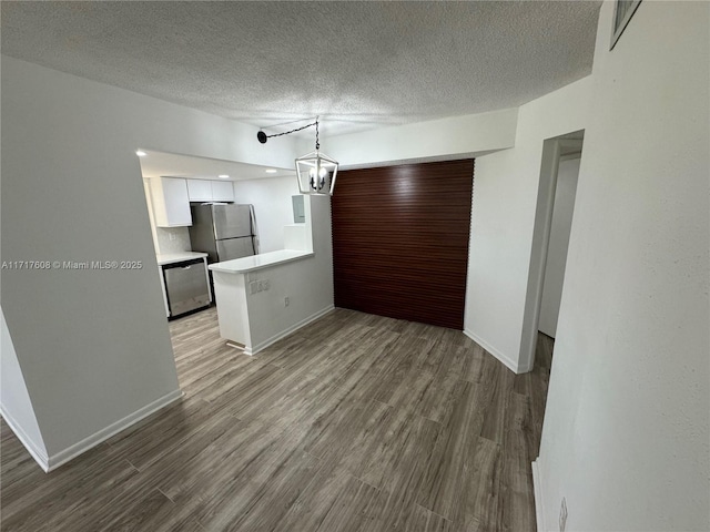 kitchen with stainless steel appliances, a textured ceiling, decorative light fixtures, white cabinets, and hardwood / wood-style flooring