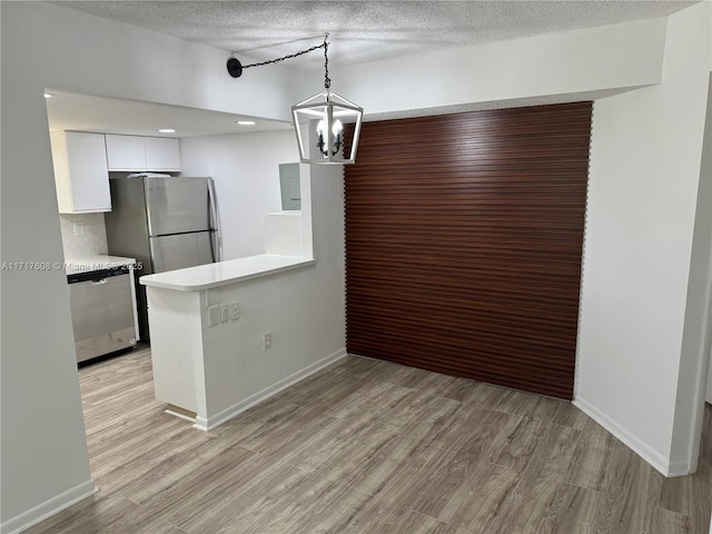 kitchen featuring appliances with stainless steel finishes, backsplash, light wood-type flooring, white cabinets, and hanging light fixtures