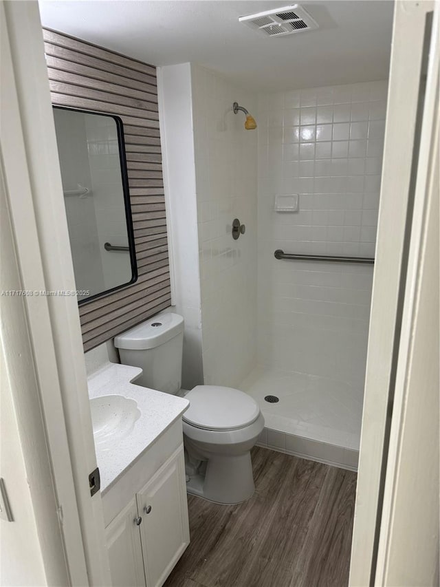 bathroom with hardwood / wood-style floors, vanity, toilet, and tiled shower