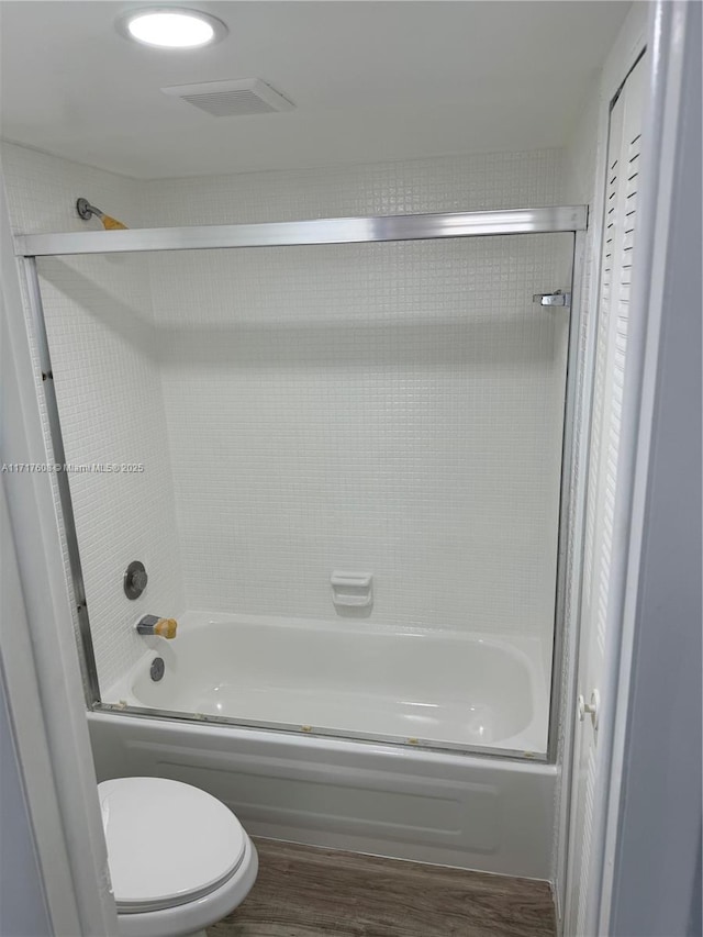 bathroom with toilet, wood-type flooring, and combined bath / shower with glass door