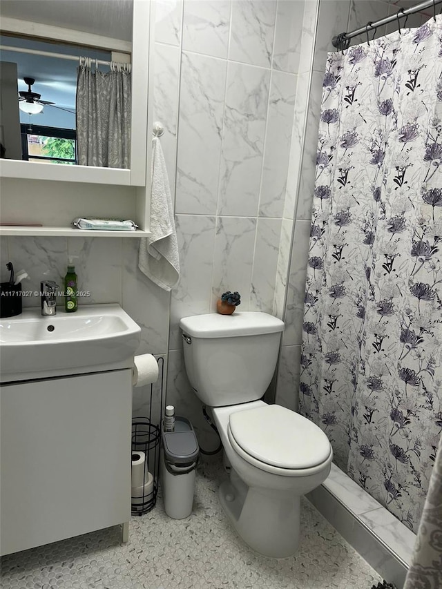 bathroom with vanity, ceiling fan, toilet, walk in shower, and tile walls