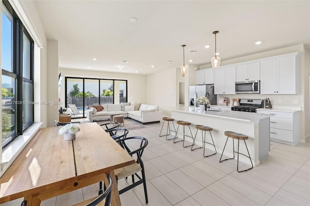 kitchen with a kitchen island with sink, hanging light fixtures, light tile patterned flooring, white cabinetry, and stainless steel appliances