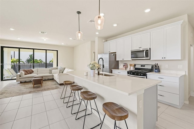 kitchen featuring a kitchen breakfast bar, stainless steel appliances, decorative light fixtures, a center island with sink, and white cabinetry