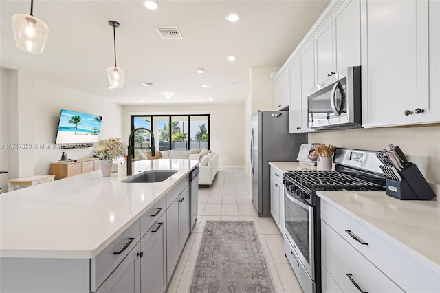 kitchen with appliances with stainless steel finishes, a kitchen island with sink, sink, white cabinetry, and hanging light fixtures