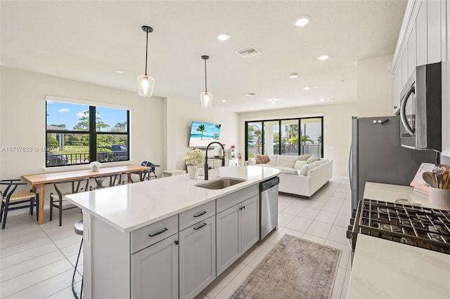 kitchen with appliances with stainless steel finishes, light stone counters, sink, a center island with sink, and decorative light fixtures