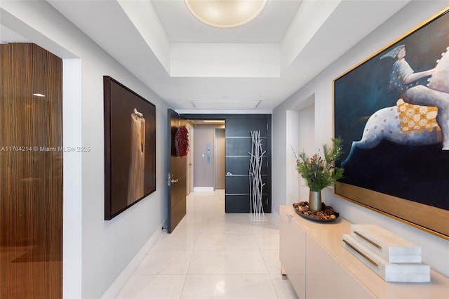 hall featuring a tray ceiling and light tile patterned flooring