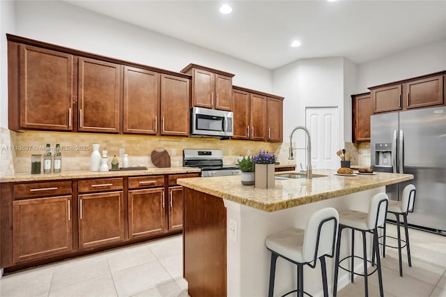 kitchen featuring light stone countertops, appliances with stainless steel finishes, decorative backsplash, sink, and a center island with sink