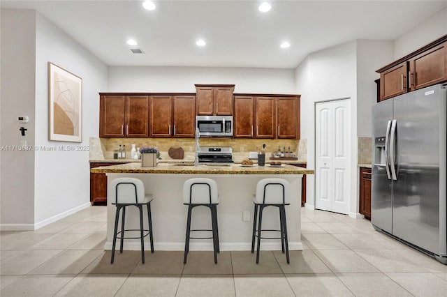 kitchen featuring light stone countertops, stainless steel appliances, light tile patterned floors, a breakfast bar area, and an island with sink