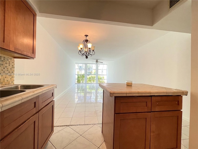 kitchen featuring tile counters, pendant lighting, decorative backsplash, light tile patterned flooring, and ceiling fan with notable chandelier