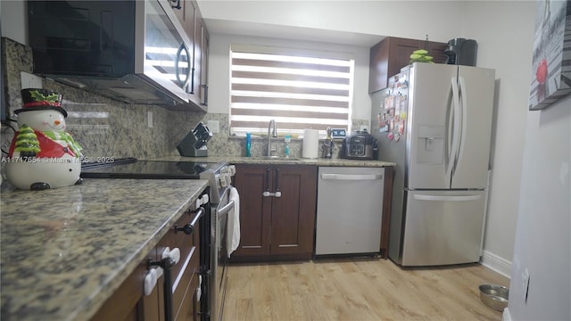 kitchen with sink, tasteful backsplash, light stone counters, appliances with stainless steel finishes, and light wood-type flooring