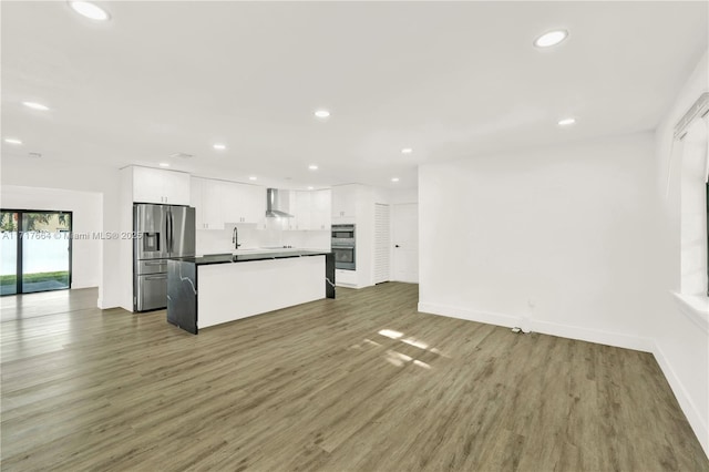 kitchen featuring white cabinetry, wall chimney exhaust hood, dark wood-type flooring, stainless steel fridge with ice dispenser, and a kitchen island with sink