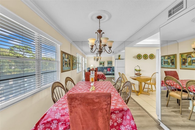 dining area featuring crown molding, light hardwood / wood-style flooring, a textured ceiling, and a notable chandelier