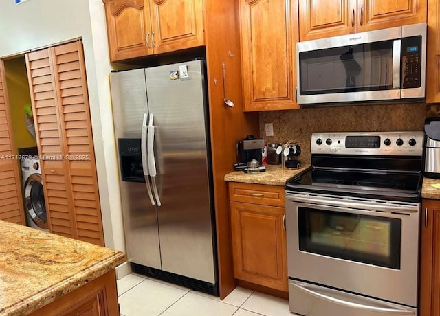 kitchen featuring light stone countertops, washer / dryer, decorative backsplash, light tile patterned floors, and appliances with stainless steel finishes