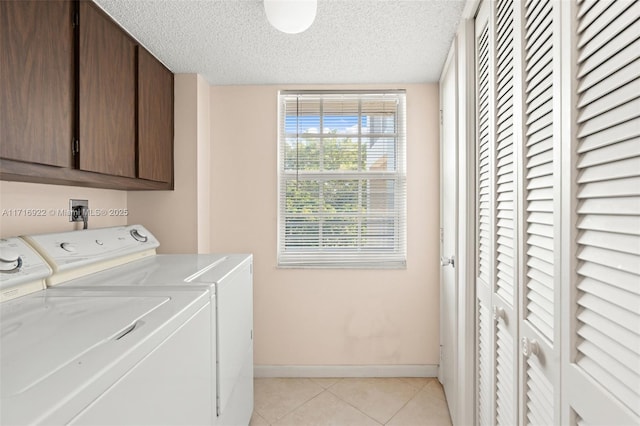 laundry area featuring cabinets, a textured ceiling, washer and clothes dryer, and light tile patterned flooring