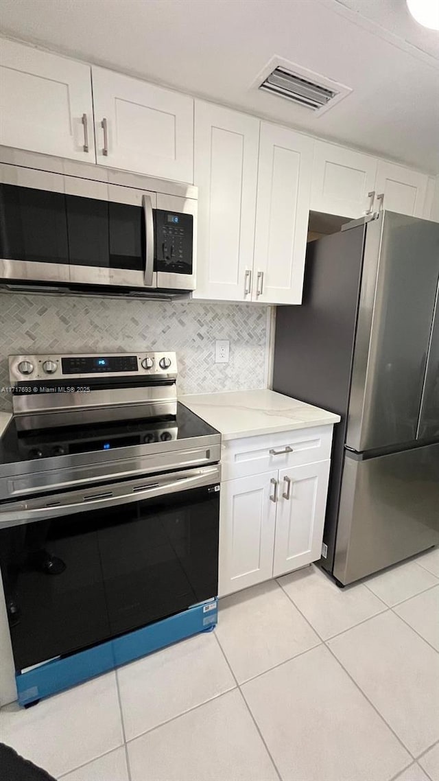 kitchen with white cabinets, light tile patterned floors, stainless steel appliances, and tasteful backsplash