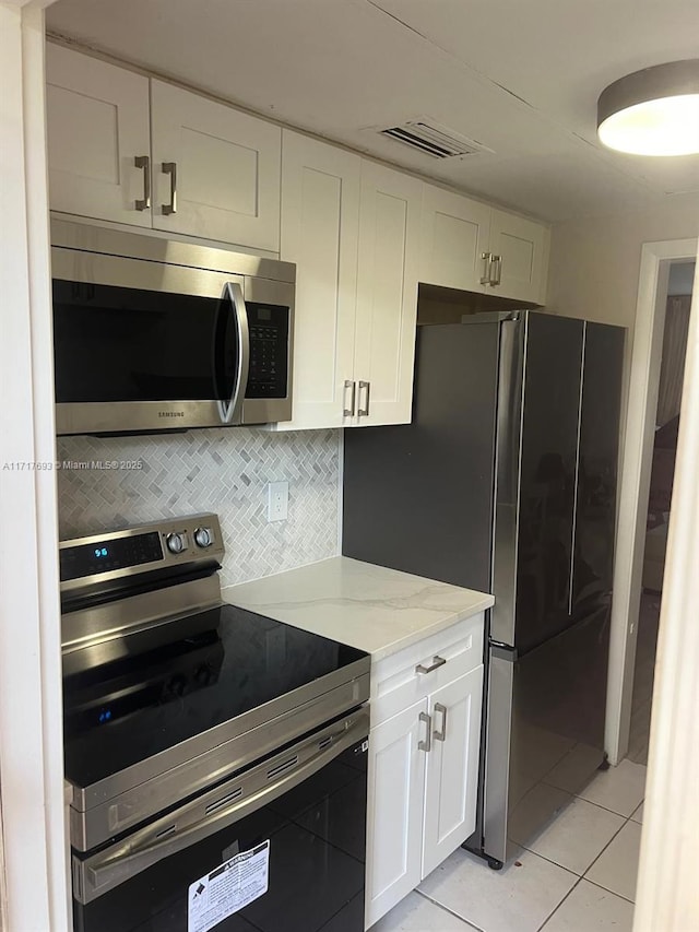 kitchen featuring light stone countertops, white cabinetry, stainless steel appliances, decorative backsplash, and light tile patterned floors