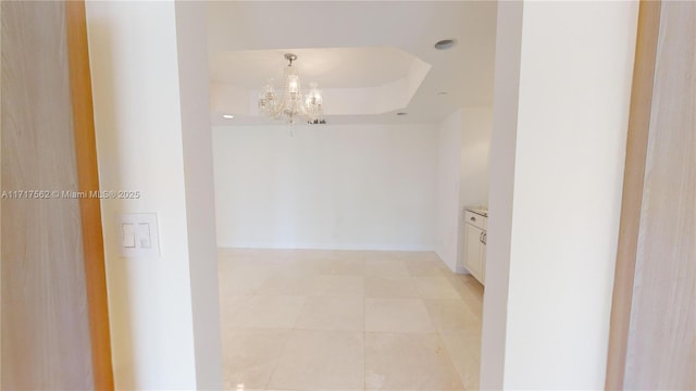 hallway with light tile patterned floors, a raised ceiling, and a notable chandelier