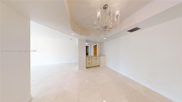 spare room with a raised ceiling, light tile patterned floors, and a notable chandelier