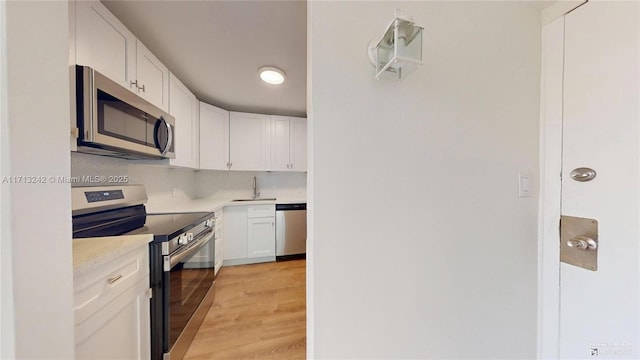 kitchen with appliances with stainless steel finishes, white cabinetry, sink, decorative backsplash, and light hardwood / wood-style floors