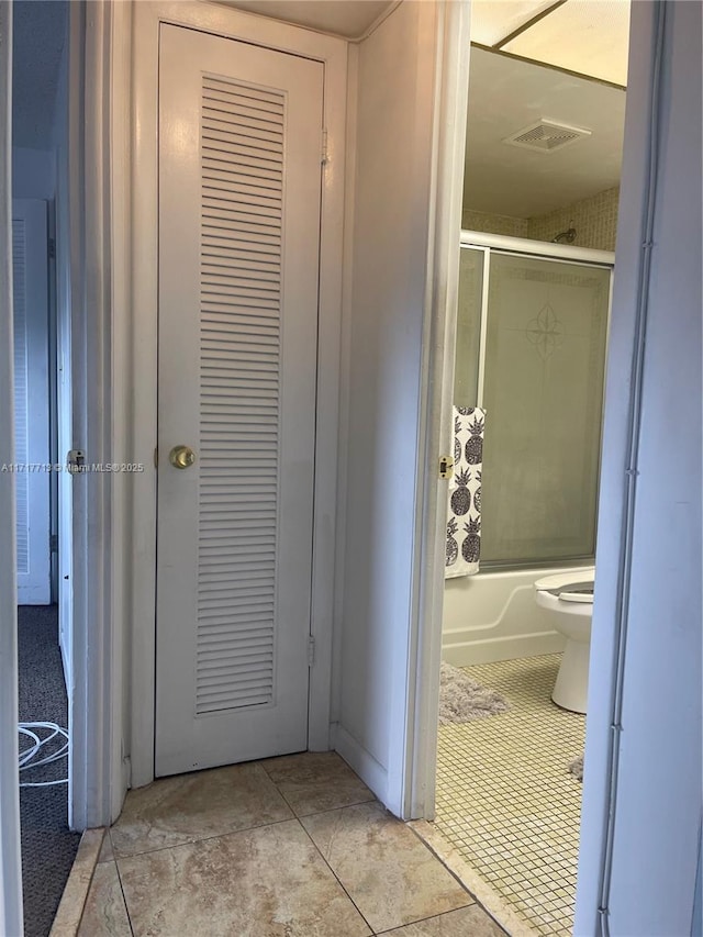 bathroom featuring toilet, tile patterned flooring, and combined bath / shower with glass door