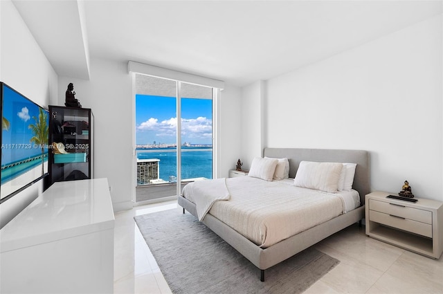 bedroom featuring access to exterior, a water view, and a wall of windows