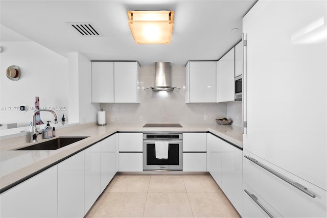 kitchen featuring appliances with stainless steel finishes, sink, wall chimney range hood, light tile patterned floors, and white cabinets