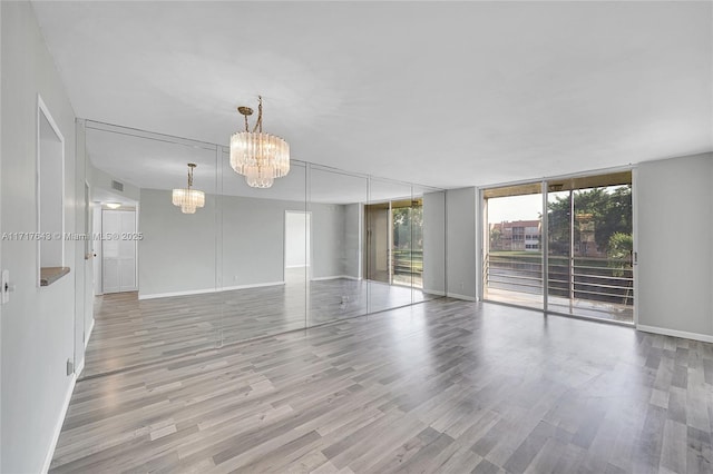 empty room with floor to ceiling windows, light wood-type flooring, and an inviting chandelier