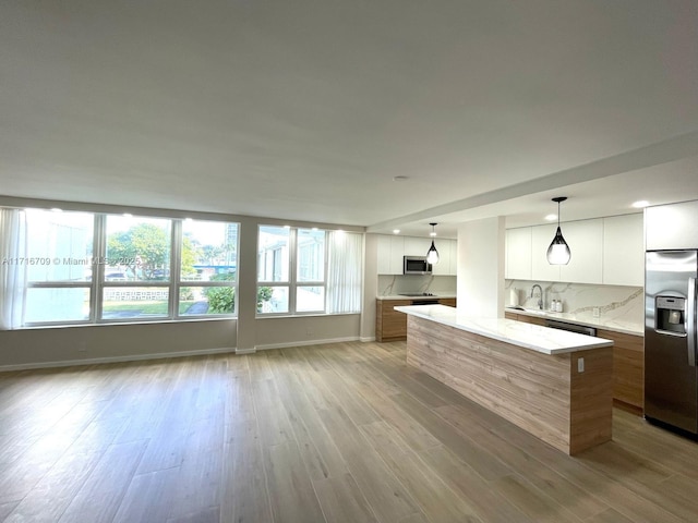 kitchen featuring backsplash, white cabinets, hanging light fixtures, light stone countertops, and stainless steel appliances