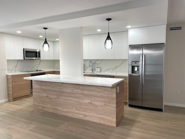 kitchen featuring a center island, white cabinets, light stone countertops, decorative light fixtures, and stainless steel appliances