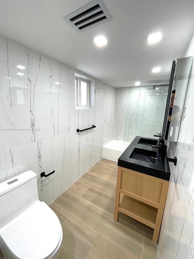 bathroom with a tile shower, vanity, toilet, and tile walls