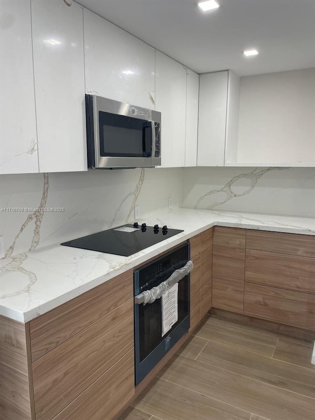 kitchen with white cabinetry, wall oven, light stone counters, backsplash, and black electric cooktop