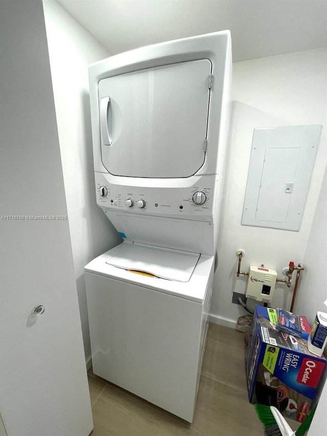 clothes washing area with electric panel and stacked washer and clothes dryer