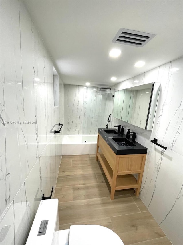 full bathroom featuring vanity, tiled shower / bath combo, tile walls, and toilet