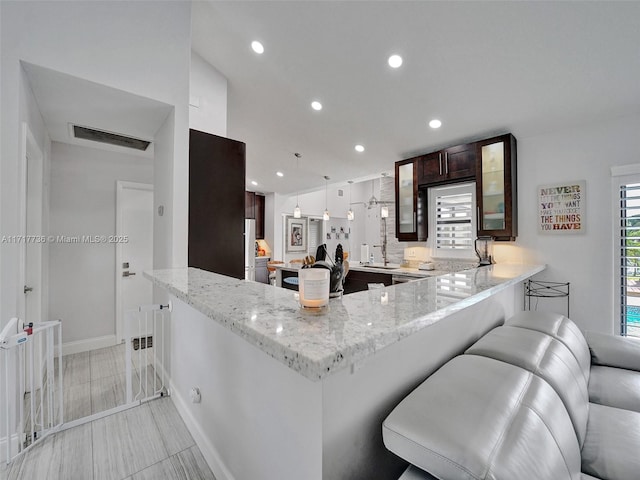 kitchen featuring light stone countertops, tasteful backsplash, kitchen peninsula, decorative light fixtures, and a breakfast bar