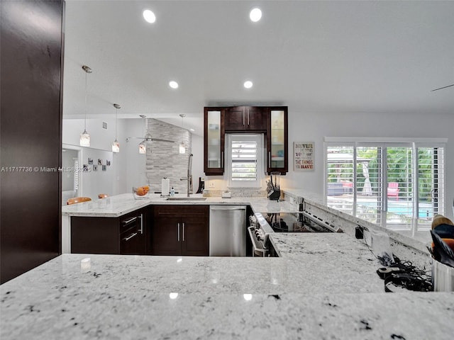 kitchen with appliances with stainless steel finishes, light stone counters, dark brown cabinets, sink, and pendant lighting