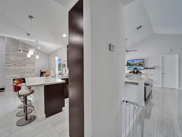 interior space featuring a kitchen bar, decorative light fixtures, vaulted ceiling, and light stone counters