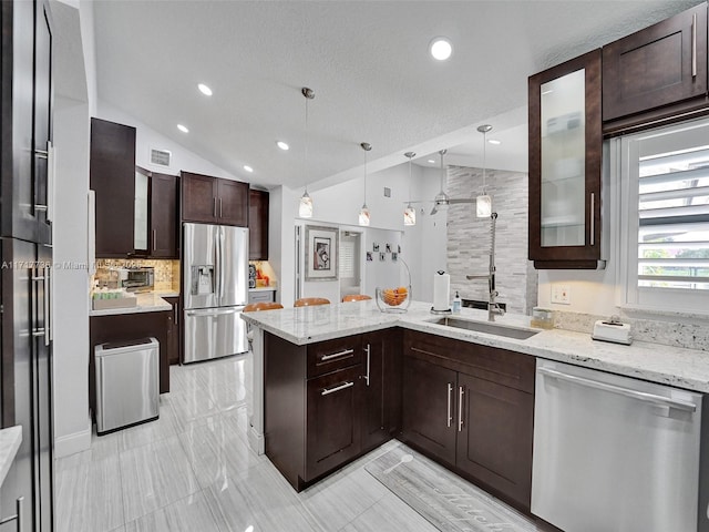 kitchen with lofted ceiling, hanging light fixtures, light stone countertops, appliances with stainless steel finishes, and kitchen peninsula