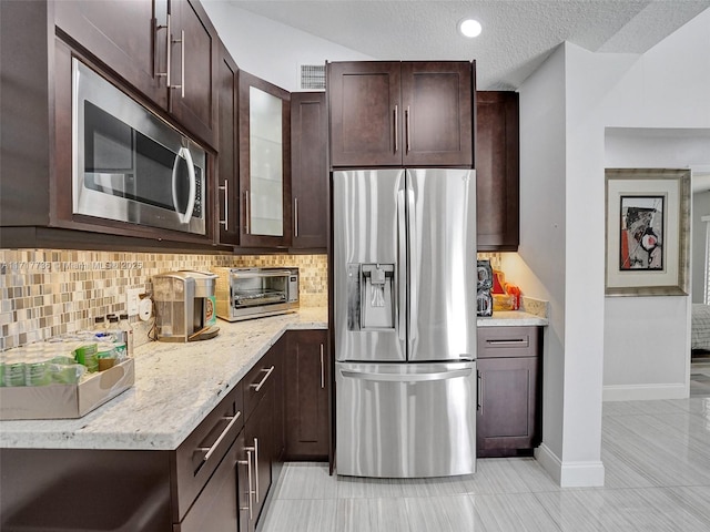 kitchen featuring dark brown cabinetry, stainless steel appliances, light stone counters, and tasteful backsplash