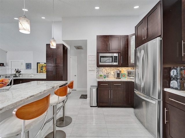 kitchen with light stone countertops, backsplash, decorative light fixtures, a breakfast bar area, and appliances with stainless steel finishes