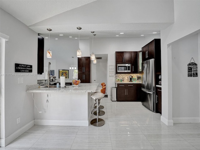 kitchen with kitchen peninsula, appliances with stainless steel finishes, a kitchen bar, light stone countertops, and hanging light fixtures