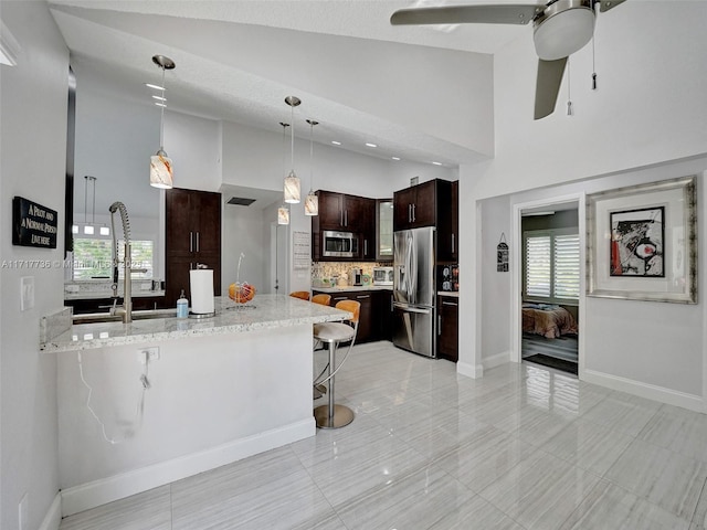 kitchen featuring high vaulted ceiling, a kitchen bar, light stone countertops, and appliances with stainless steel finishes