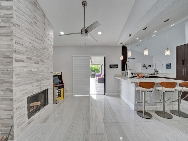 kitchen featuring a kitchen breakfast bar, a stone fireplace, decorative light fixtures, light stone counters, and kitchen peninsula