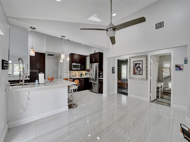 kitchen with a kitchen breakfast bar, pendant lighting, decorative backsplash, dark brown cabinets, and appliances with stainless steel finishes