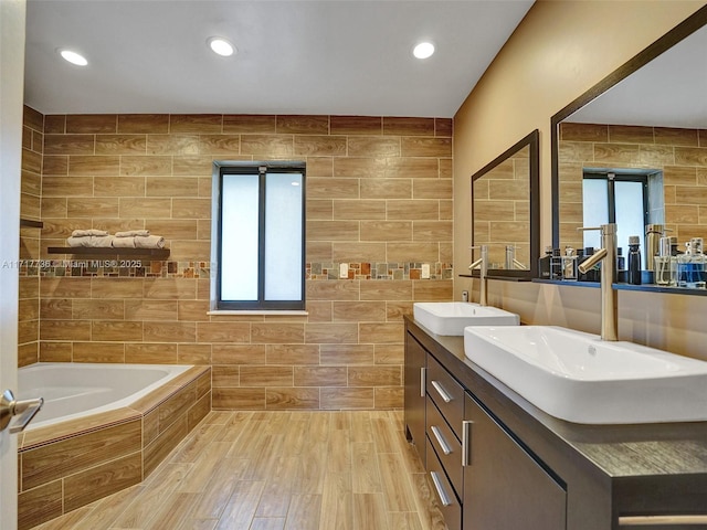 bathroom featuring vanity, a relaxing tiled tub, and tile walls