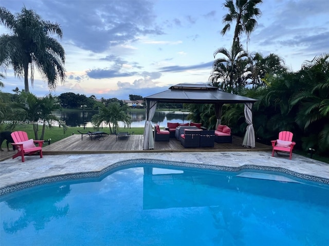 pool at dusk featuring a gazebo, a deck with water view, and outdoor lounge area