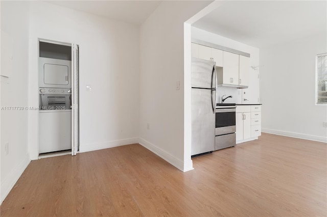 kitchen featuring stove, light wood-type flooring, white cabinets, stainless steel refrigerator, and stacked washer / drying machine