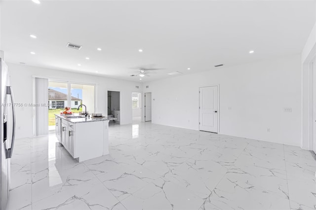 kitchen featuring stainless steel refrigerator with ice dispenser, ceiling fan, sink, white cabinetry, and an island with sink