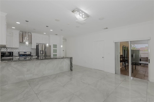 interior space featuring wall chimney exhaust hood, dark stone countertops, decorative light fixtures, white cabinets, and appliances with stainless steel finishes