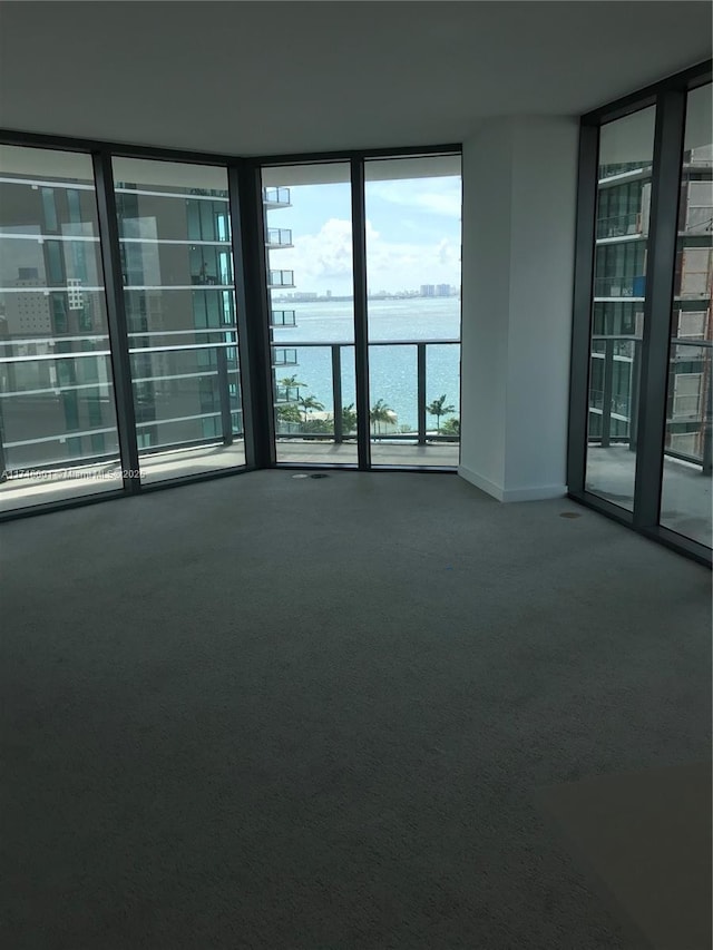 carpeted spare room with floor to ceiling windows and a water view