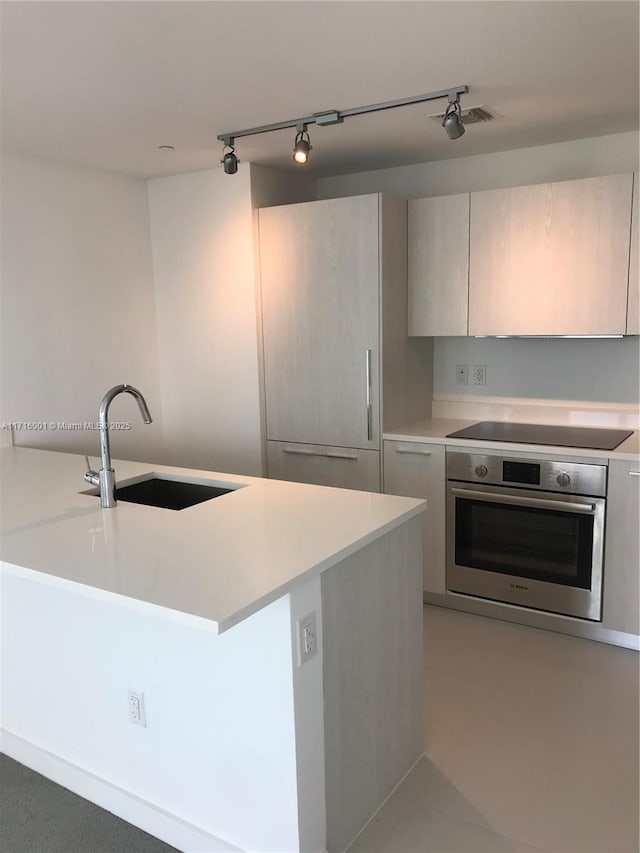 kitchen featuring stainless steel oven, track lighting, black electric stovetop, sink, and tile patterned flooring